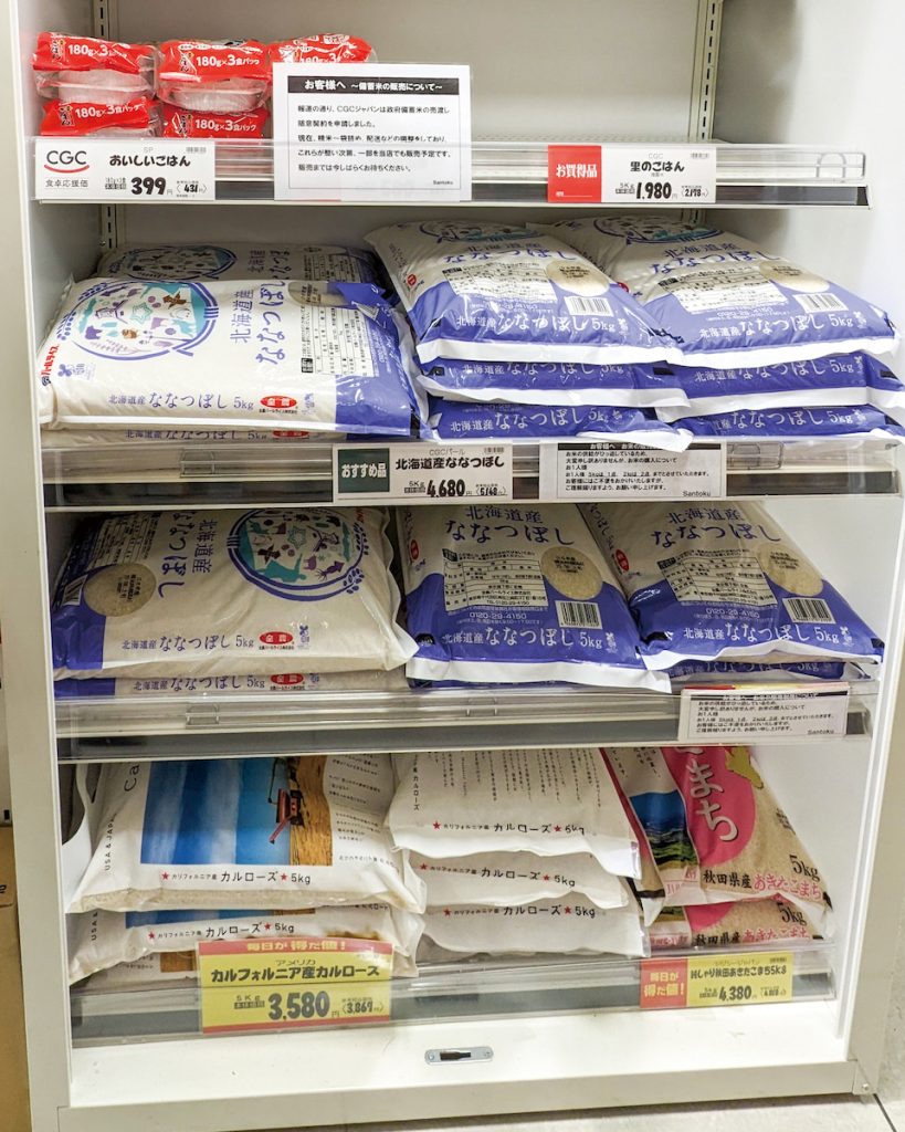 日本藉由釋出低價的儲備米（圖中空架處）及進口米（如圖中貨架底部美國加州米）等方式調節米價，但其中流通狀況、衍生的政治風波臺灣可引以為戒。