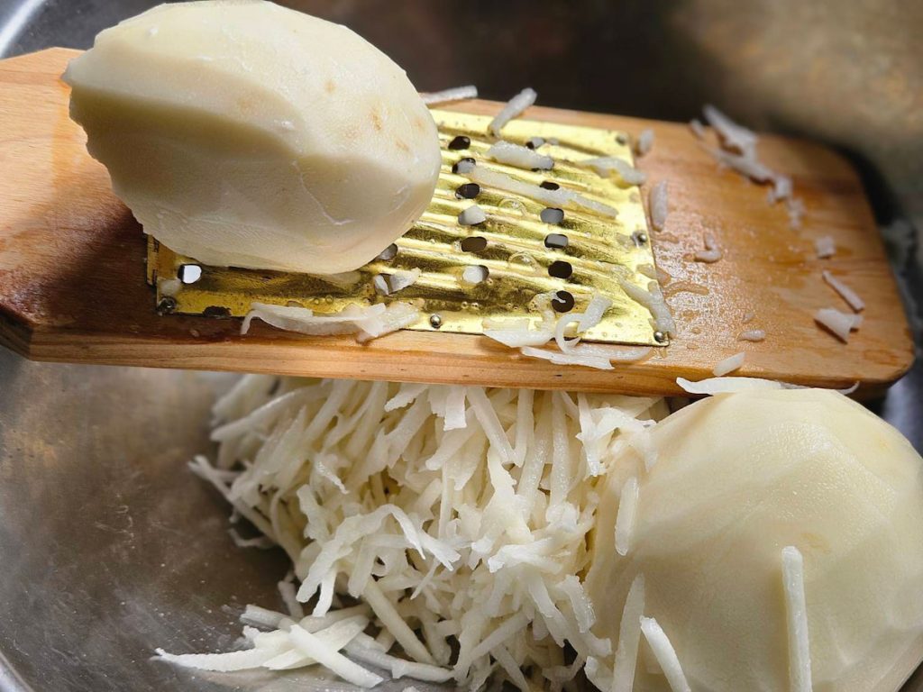 1 馬鈴薯洗淨削皮，以菜礤將馬鈴薯礤成粗簽，太長的粗簽要用剪刀剪短，以免煎餅不好塑型。
2 打入一顆蛋、一小匙鹽、一小匙胡椒粉，攪拌均勻，馬鈴薯會逐漸出水，水分千萬不要倒掉，裡面有豐富的澱粉，是煎餅成型的關鍵。
