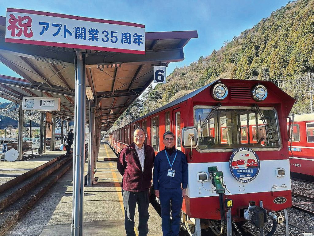 大井川鐵道鳥塚亮社長與井川線滝山站長,於掛有姊妹鐵道紀念牌的守車前合影。(大井川鐵路提供)