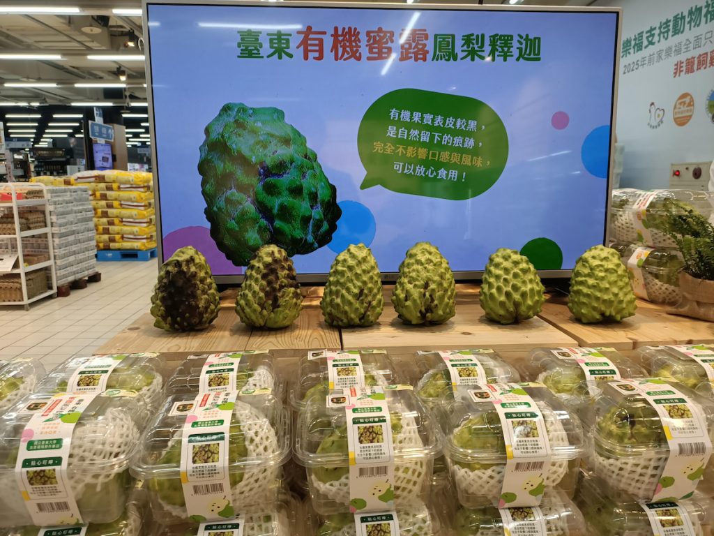 有機鳳梨釋迦果皮上的黑斑，多為自然生長與粉介殼蟲活動留下的痕跡，通常不影響果肉品質與風味。圖為賣場向消費者說明有機果實的外觀特色。